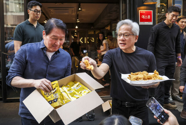 젠슨 황 엔비디아 CEO(오른쪽)와 최태원 SK 회장이 7일 서울 강남구 깐부치킨 삼성점에서 치맥회동 도중 시민들에게 세븐일레븐의 HBM칩과 치킨을 나눠주고 있다. /뉴시스